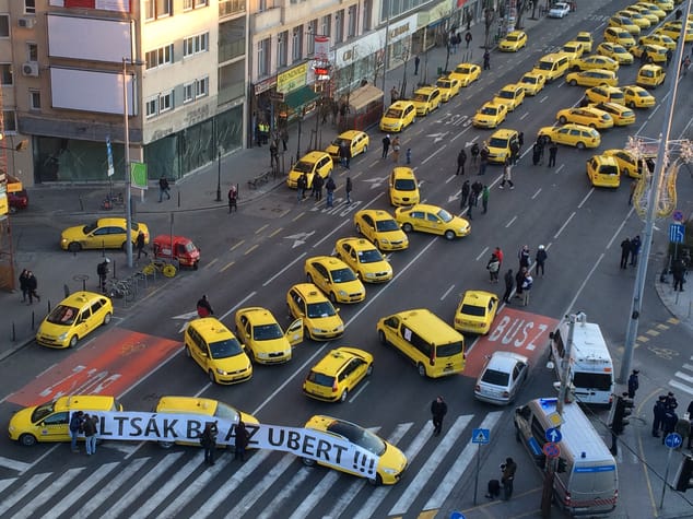 Budapest taxis drivers block traffic as they protest demanding a ban on Uber in downtown Budapest, Hungary, Jan. 18, 2018. More than 100 taxis blocked traffic in downtown Budapest as drivers demanded a ban on Uber and other ride-hailing apps. The yellow vehicles from several taxi companies blocked off a key intersection near St. Stephen's Basilica in the Hungarian capital, causing significant traffic delays. Banner reads in Hungarian: Ban Uber! (AP Photo/Bela Szandelszky)